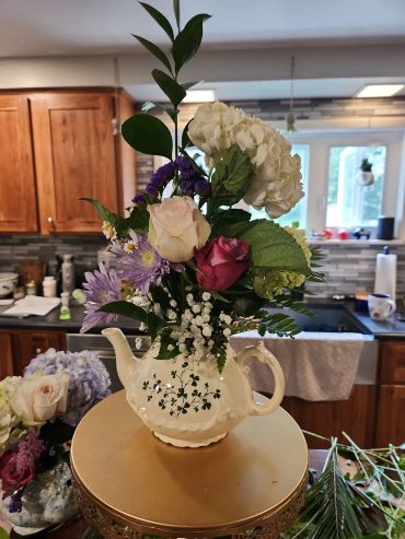 Floral arrangement in a decorative teapot on a kitchen table.