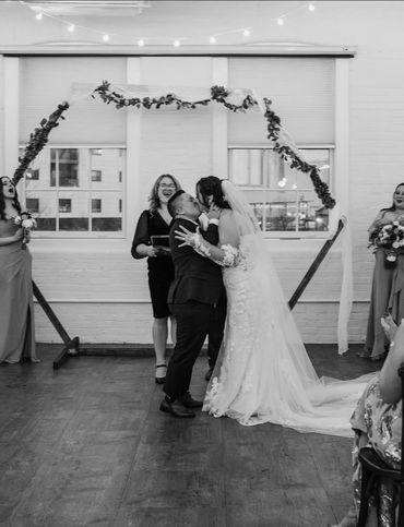 A couple shares a kiss during their wedding ceremony indoors.