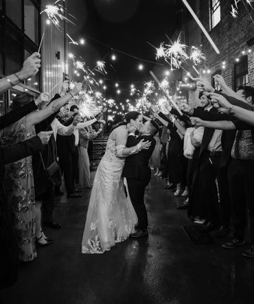 Newlyweds share a kiss amid guests holding sparklers in celebration.