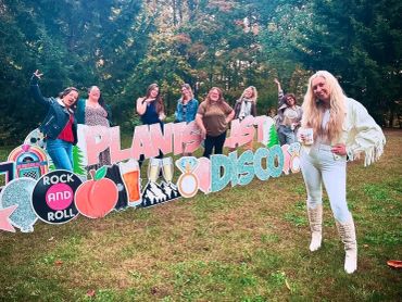 Group of women posing happily outdoors with a colorful "Plants Last Disco" sign.