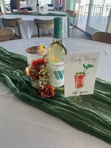Table setup with a wine bottle, decorative flowers, and a Bloody Mary sign.