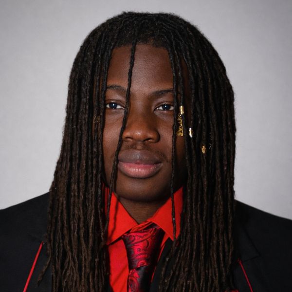 Young man with long dreadlocks wearing a black suit and red tie.