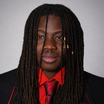 Young man with long dreadlocks wearing a black suit and red tie.