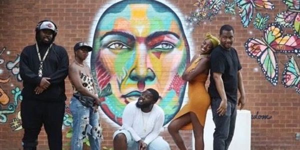 Five people posing in front of a colorful mural of a face with butterflies.