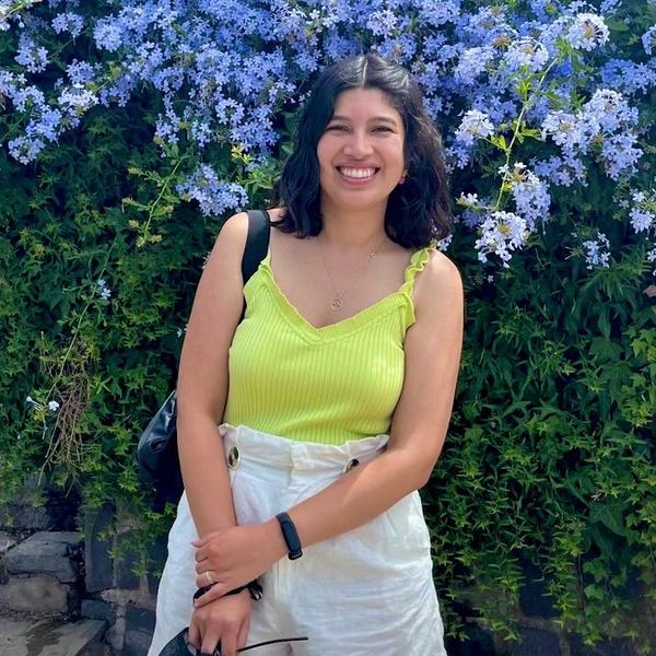 Mujer sonriente frente a flores púrpuras.