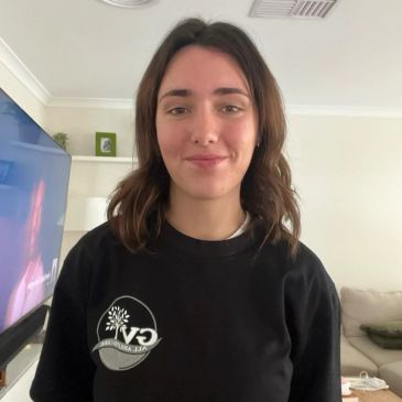 A woman smiling indoors wearing a black sweatshirt with a logo.