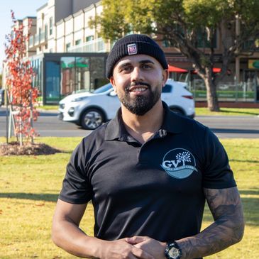 Smiling man wearing a black beanie and polo shirt outdoors in a sunny park.