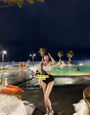 Woman posing by a lit outdoor pool at night.