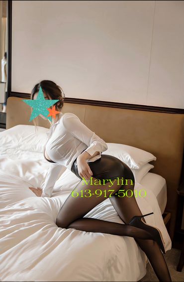 Woman in white shirt and black skirt posing on bed.