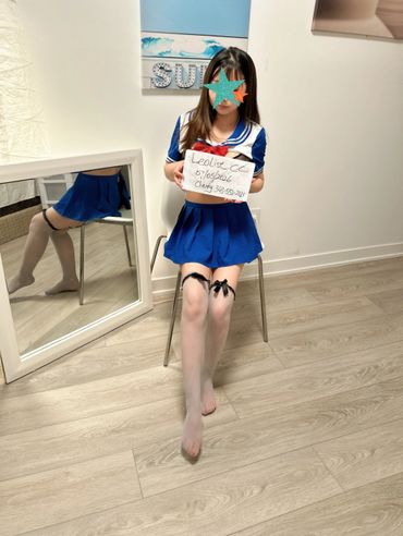 Young woman in blue sailor-style outfit sitting on a chair indoors.