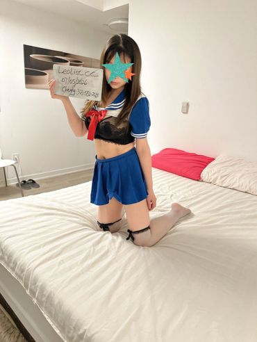 Person in a blue sailor outfit kneeling on a bed, holding a sign.