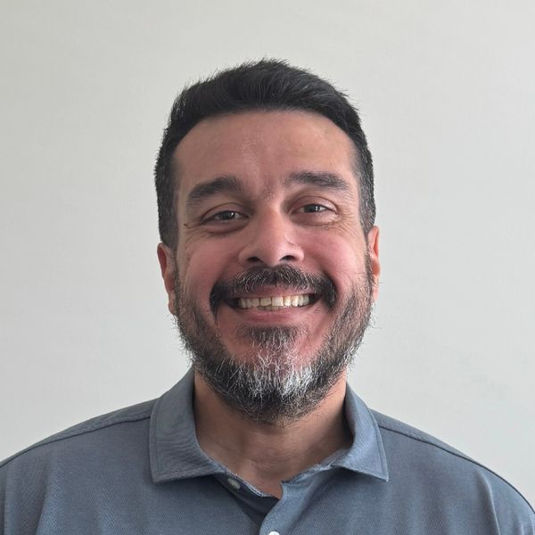 A man with a beard smiling warmly against a plain background.