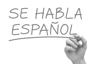 Mano escribiendo "SE HABLA ESPAÑOL" en pizarra.