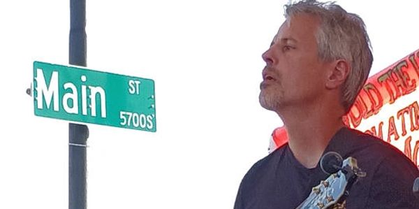 Man playing guitar near a Main Street sign.