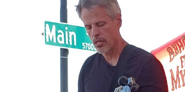 Man playing guitar near a Main Street sign.