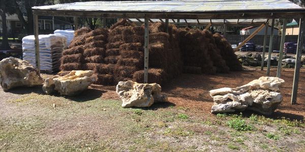 Shelter storing stacked mulch bags and large rocks outdoors.