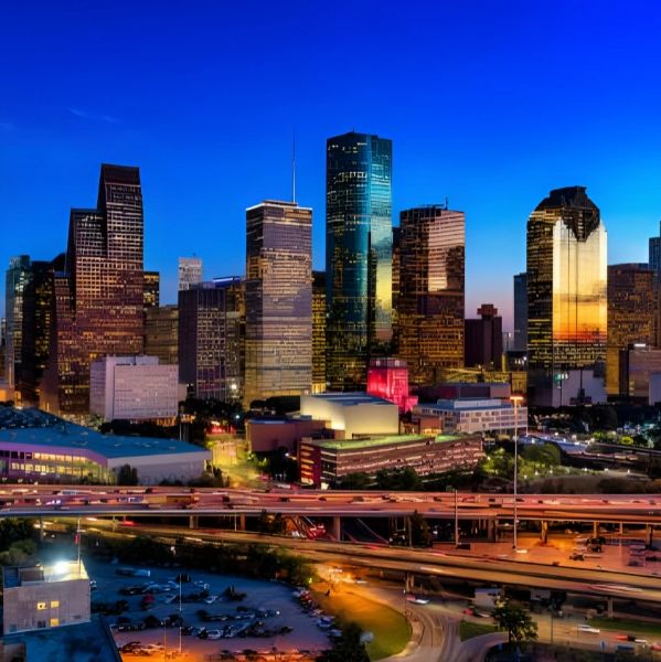 City skyline at dusk with illuminated buildings and highways.