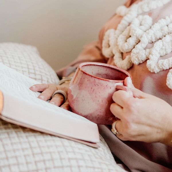 Person relaxing with a pink mug and book, wearing cozy knit clothing.