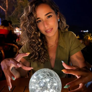 Woman with curly hair posing with a glowing orb at night.