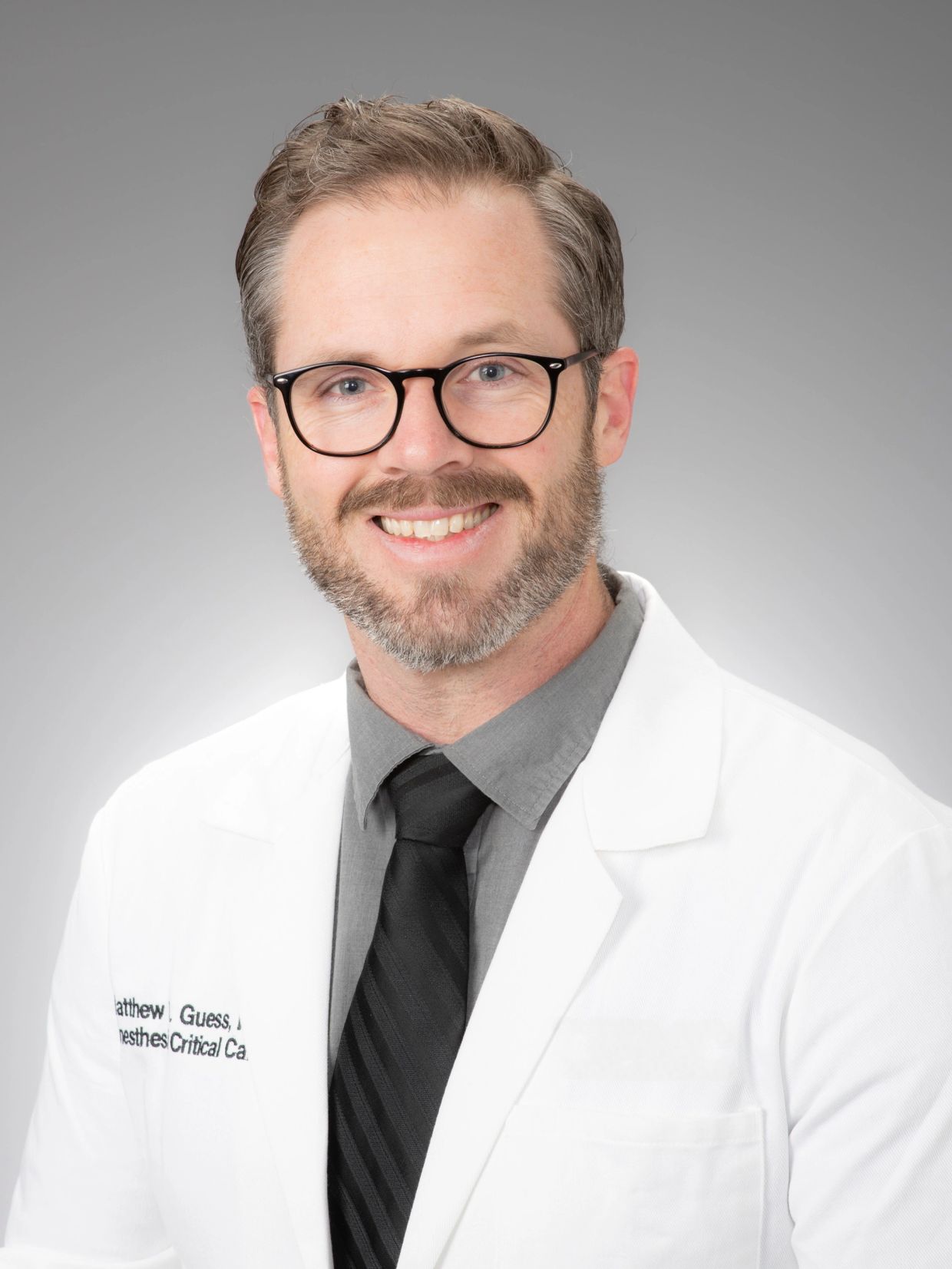 Smiling male doctor in white coat and glasses.