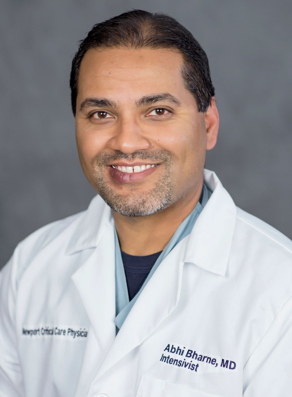 Smiling male doctor in white coat with name and title embroidered.