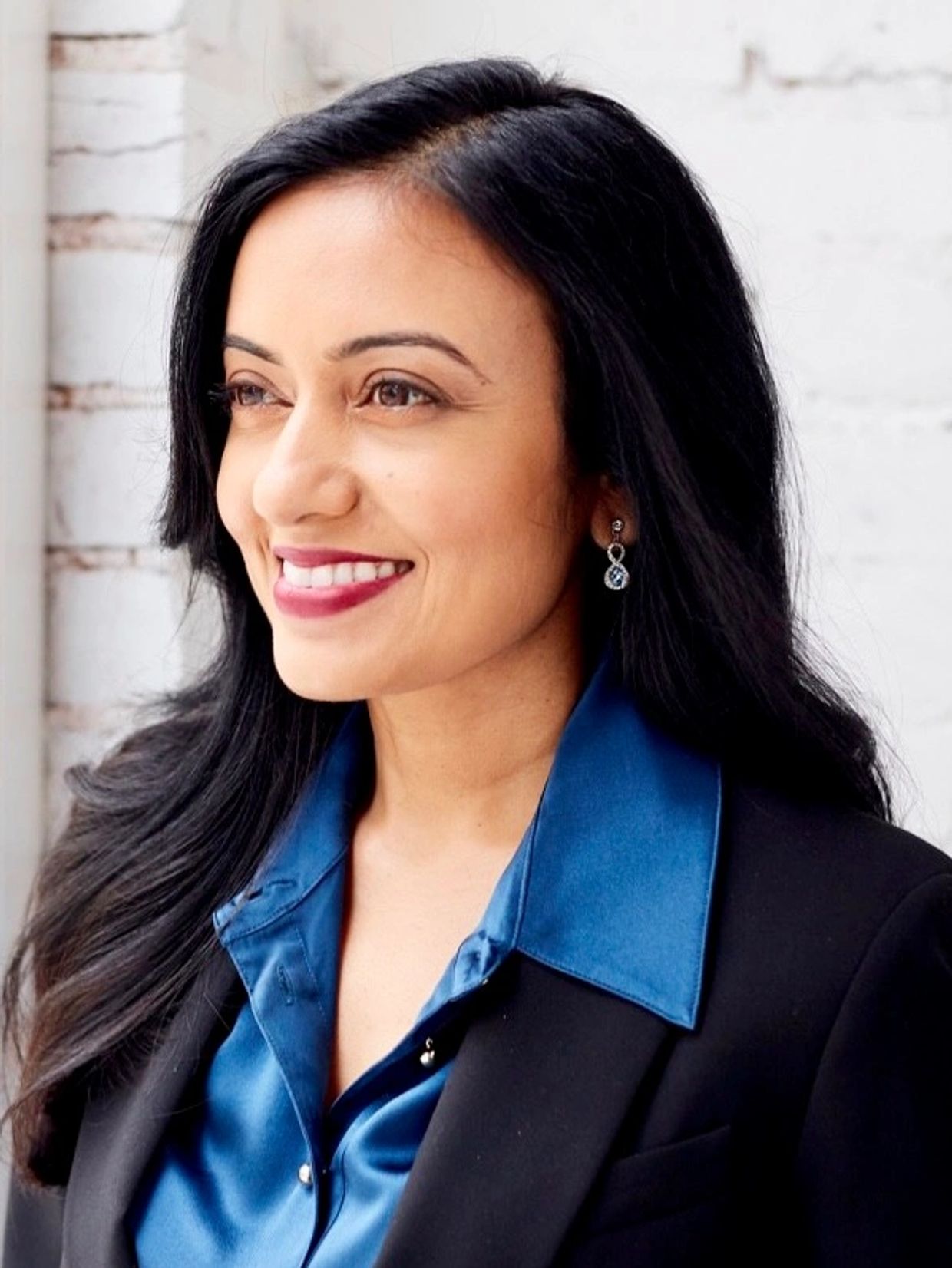Confident woman smiling, wearing a blue silk shirt and black blazer.