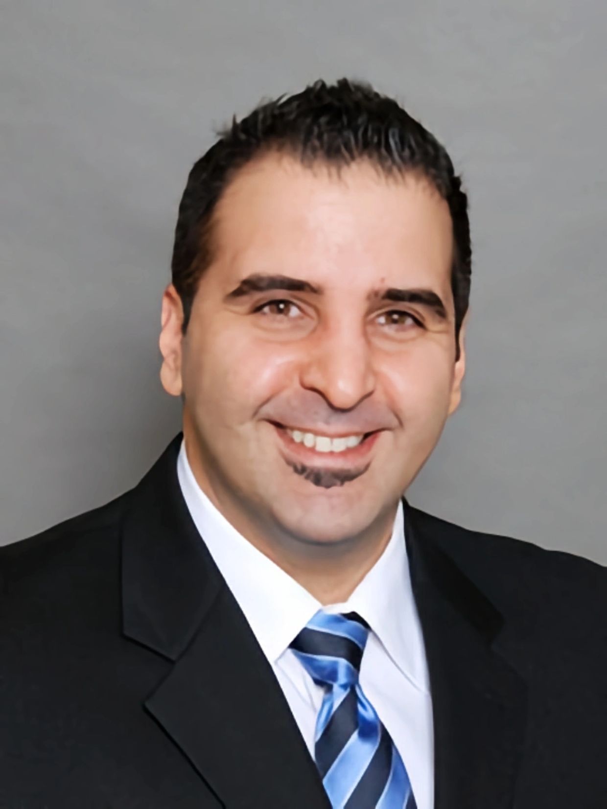 Man in suit smiling against gray background.