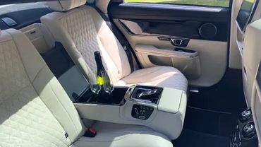 Luxurious car backseat with beige leather seats and a center console holding a wine bottle and glasses.