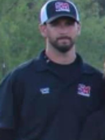 Man in a black shirt and cap outdoors.