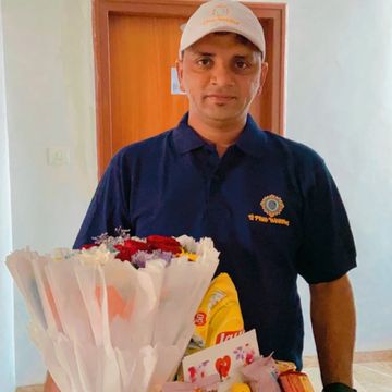 A man in a blue shirt and white cap standing behind a table with flowers and snacks.