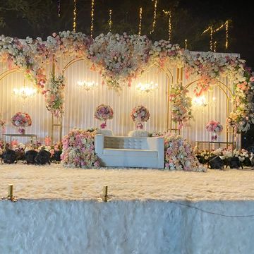 Elegant floral wedding stage with white seating and warm lighting.