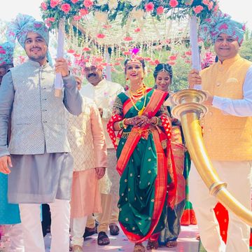 Bride in green saree with family under floral canopy at traditional wedding.