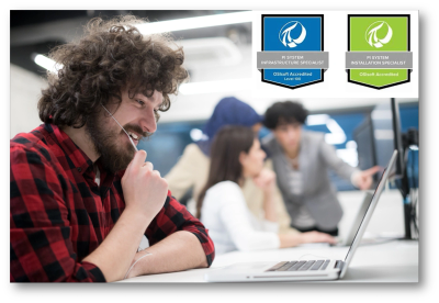 Young man working on a laptop with colleagues in the background in an office setting.
