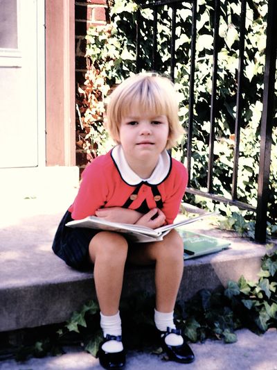 A young girls sitting on a porch with an open book.