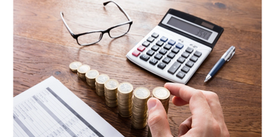 Person stacking coins with calculator and financial documents on desk.