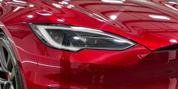 Close-up of a red sports car's sleek headlight and front fender.