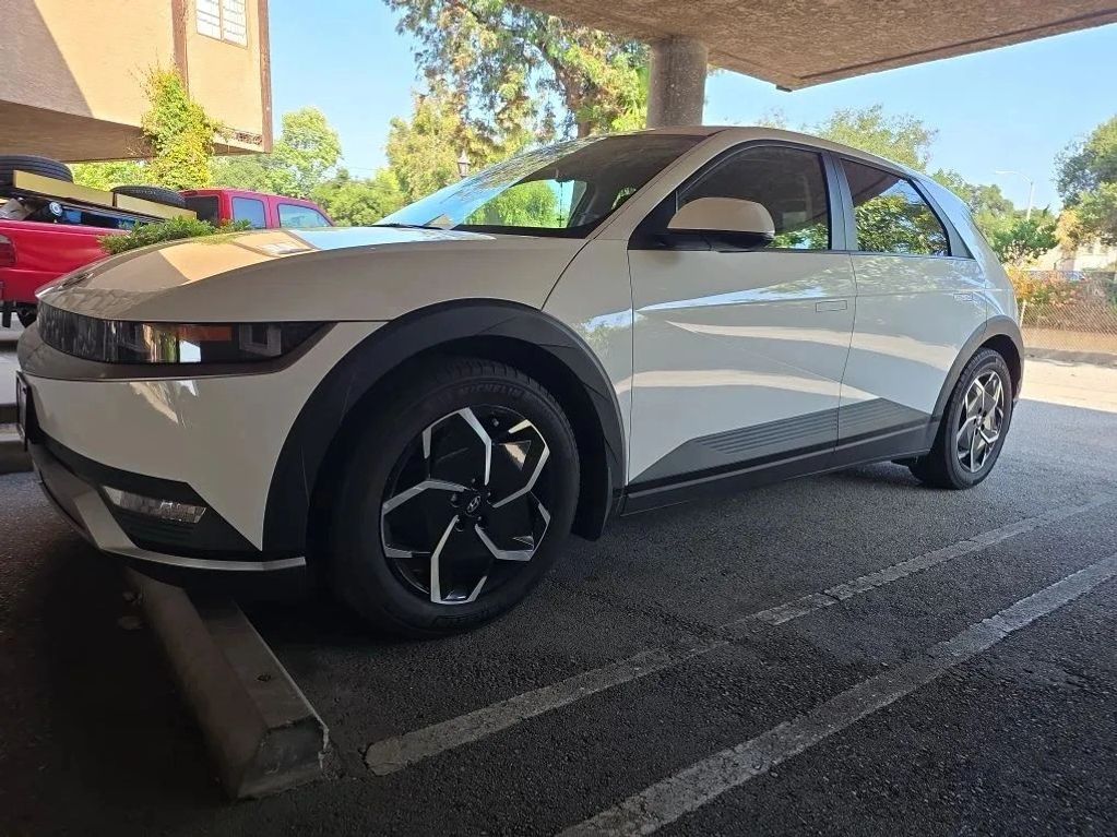 White modern electric hatchback car parked in a shaded parking spot.