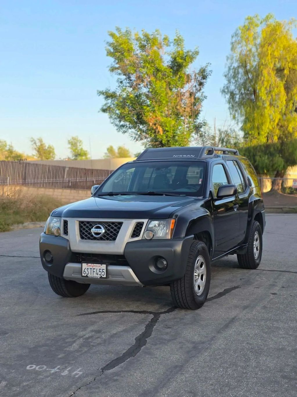 Black Nissan SUV parked on a cracked asphalt road with greenery in the background.