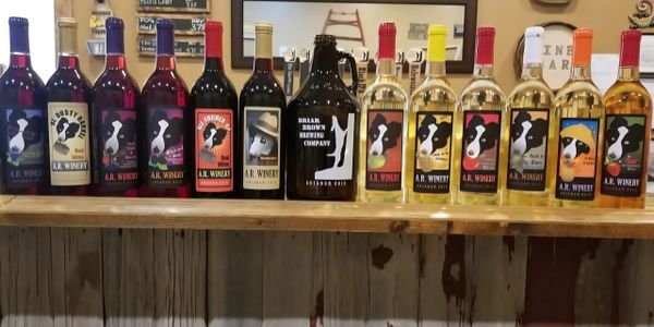 Variety of red and white wines from A.R. Winery displayed on a wooden shelf.
