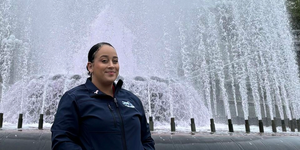 Lisberry posing in front of a large water fountain wearing a navy jacket.