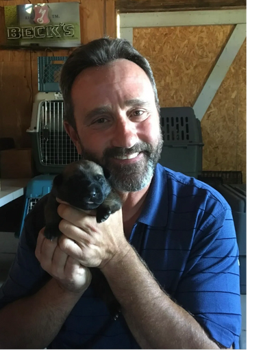 a man holding a puppy and smiling 