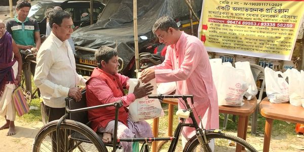 A man in pink distributes food to a person in a wheelchair during a community event.