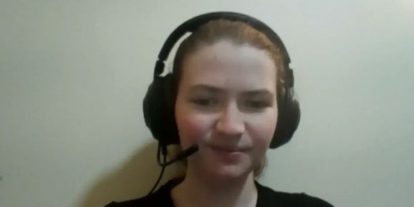 Young woman wearing a headset with microphone against a plain wall.