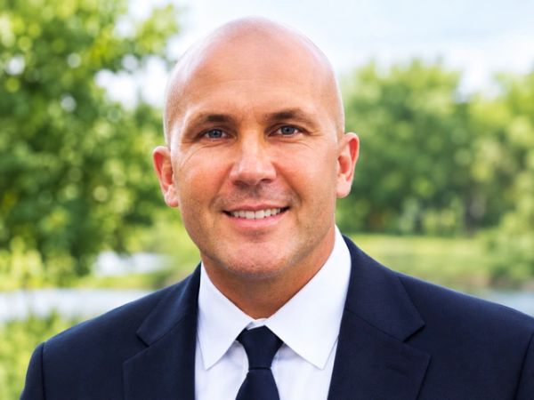 Smiling bald man in a suit and tie outdoors.