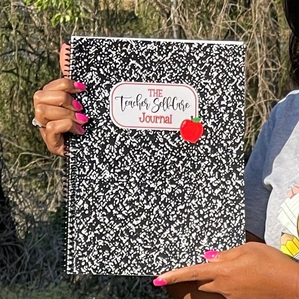 Person holding a black and white spiral notebook titled 'The Teacher Self-Care Journal.'