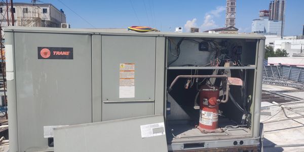 Open Trane HVAC unit on rooftop with visible compressor and wiring.