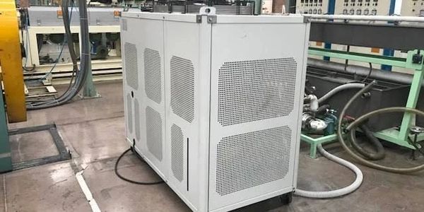 White industrial machine in a factory setting with pipes and control panels.
