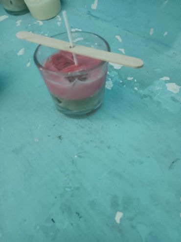 A candle-making setup with wax in a glass and a wick held by a wooden stick.