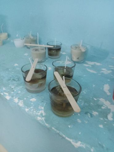 Small glass containers with wax and sticks on a chipped blue surface.