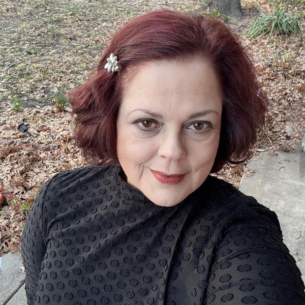 Middle-aged woman with red hair and black textured sweater outdoors.